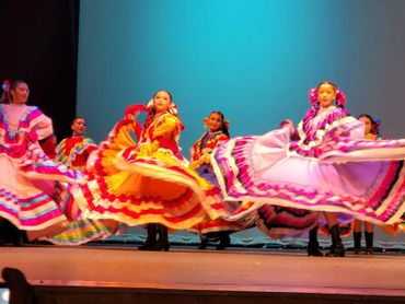 Dancers in colorful traditional dresses perform on stage with flowing skirts.