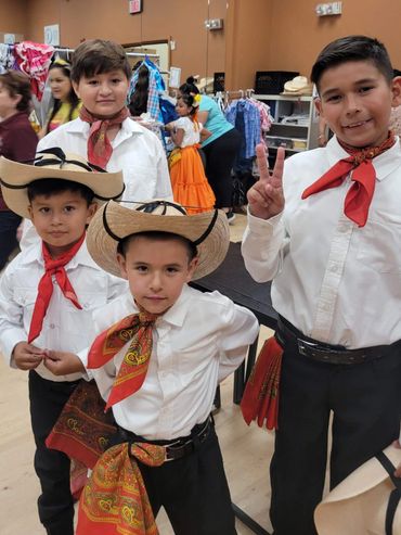 Four boys dressed in traditional cowboy attire with hats and red scarves.