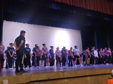 A large group of performers stands on stage during a rehearsal or event.