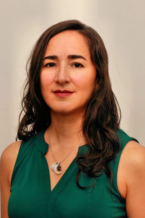 Confident woman with long dark hair wearing a green sleeveless top.