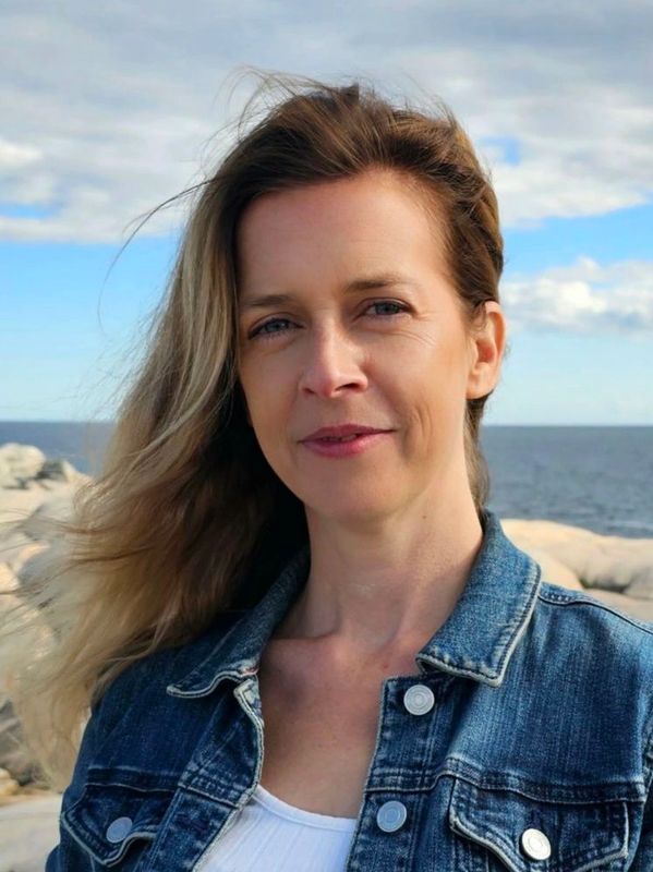 Woman with blonde hair wearing a denim jacket by the seaside.