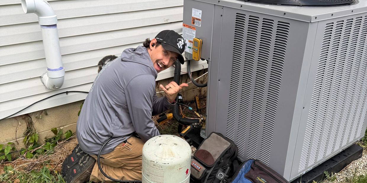Technician smiling while repairing an HVAC unit outside a house.