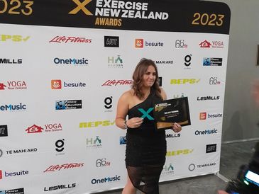 Woman in black dress holding an award at Exercise New Zealand 2023.