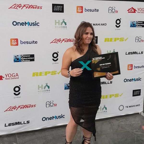 Woman in black dress holding an award plaque at a fitness event.