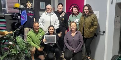 Group photo of seven people posing inside a gym with workout gear and mannequins.