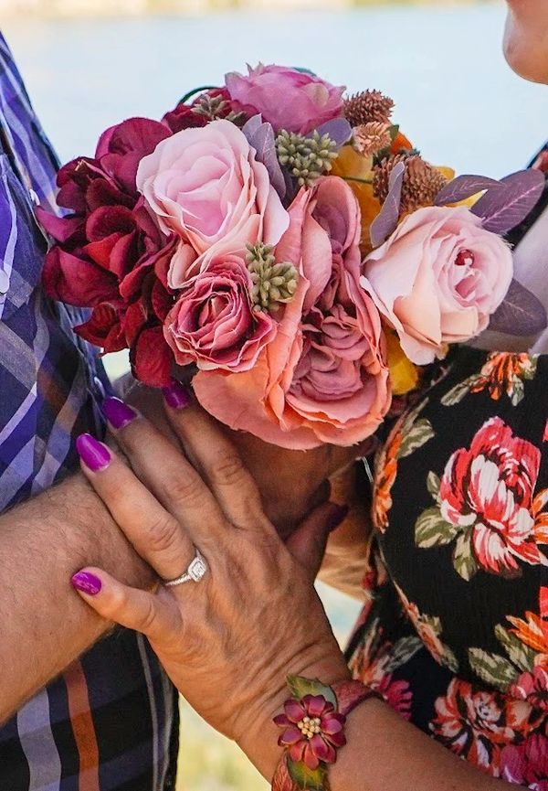 Couple holding hands with a vibrant bouquet of roses and floral dress details.