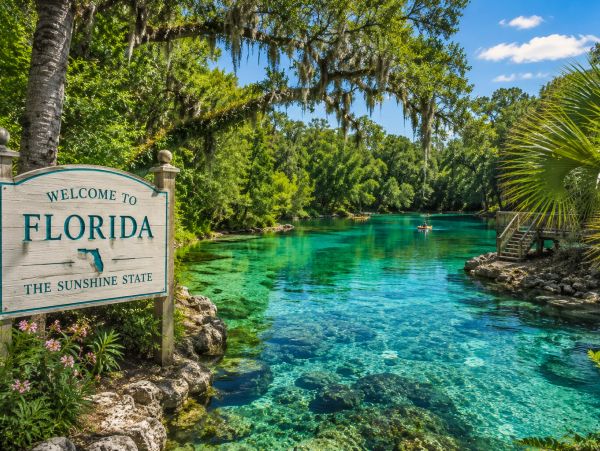 Welcome sign by a clear blue river in lush Florida nature.