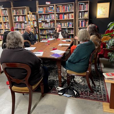 A group of people engaged in a discussion around a wooden table in a cozy library.