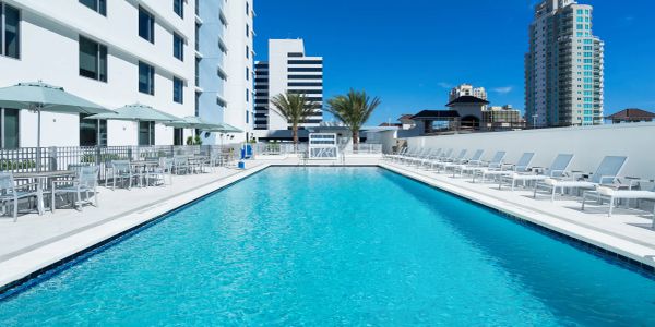 A rooftop swimming pool with lounge chairs and umbrellas under a clear blue sky.
