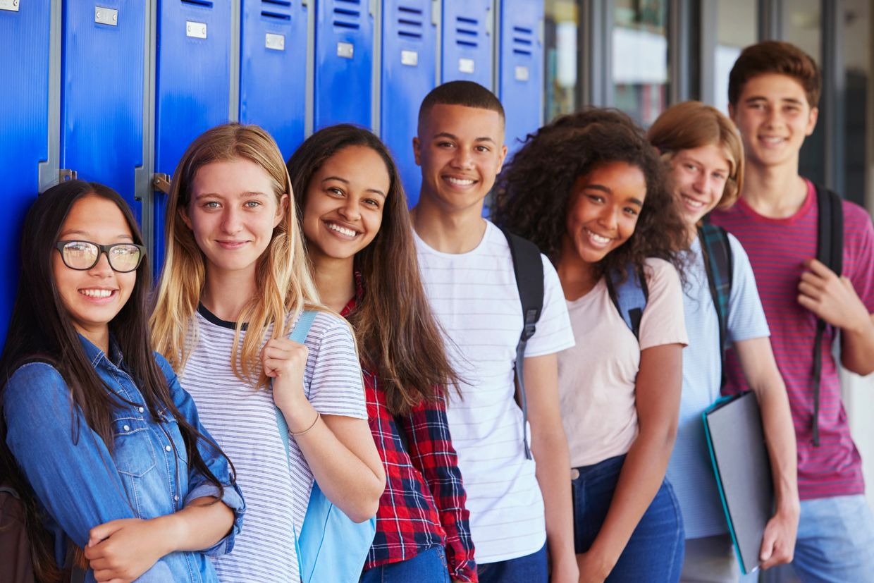 A diverse group of smiling students standing by blue lockers in a school hallway.