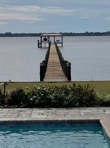 Pool and dock overlooking a calm lake under a cloudy sky.