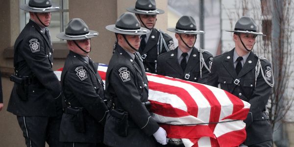 Uniformed officers carrying a flag-draped casket during a solemn ceremony.