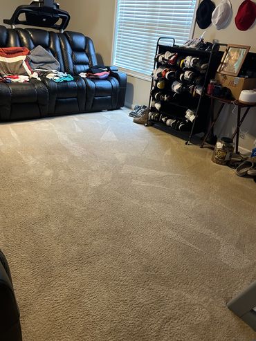 A cozy room with a black leather couch, shoe rack, and a carpeted floor.