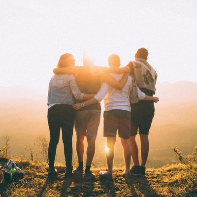 Four friends stand arm-in-arm watching a sunset over hills.