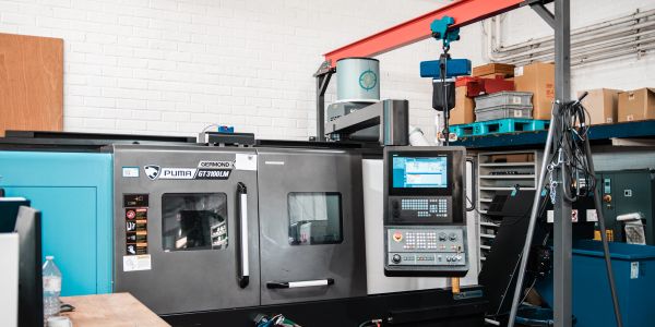 Industrial CNC machine in a workshop with control panel and storage shelves.