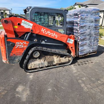Kubota SVL 75-2 loader carrying landscaping mulch bags.