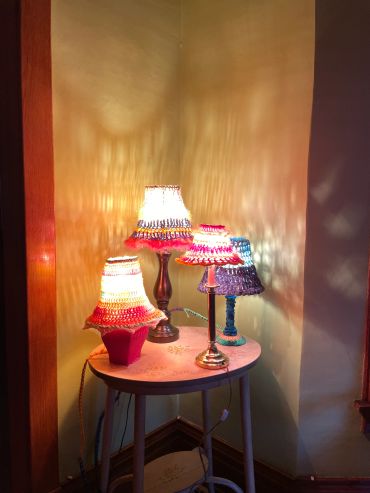 Four colorful, crocheted lamp covers on a round table.