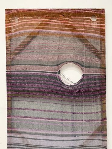 Colorful woven textile with geometric shapes and a central hole.