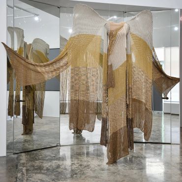 Ethereal knitted garment displayed in front of mirrors.