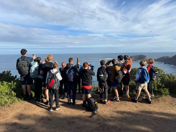 Group of people with backpacks overlooking the ocean on a clear day.