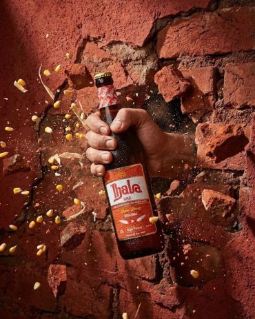 Hand holding a beer bottle breaking through a brick wall.