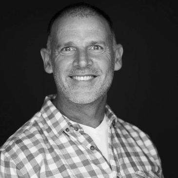 Black and white portrait of a smiling man in a checkered shirt.