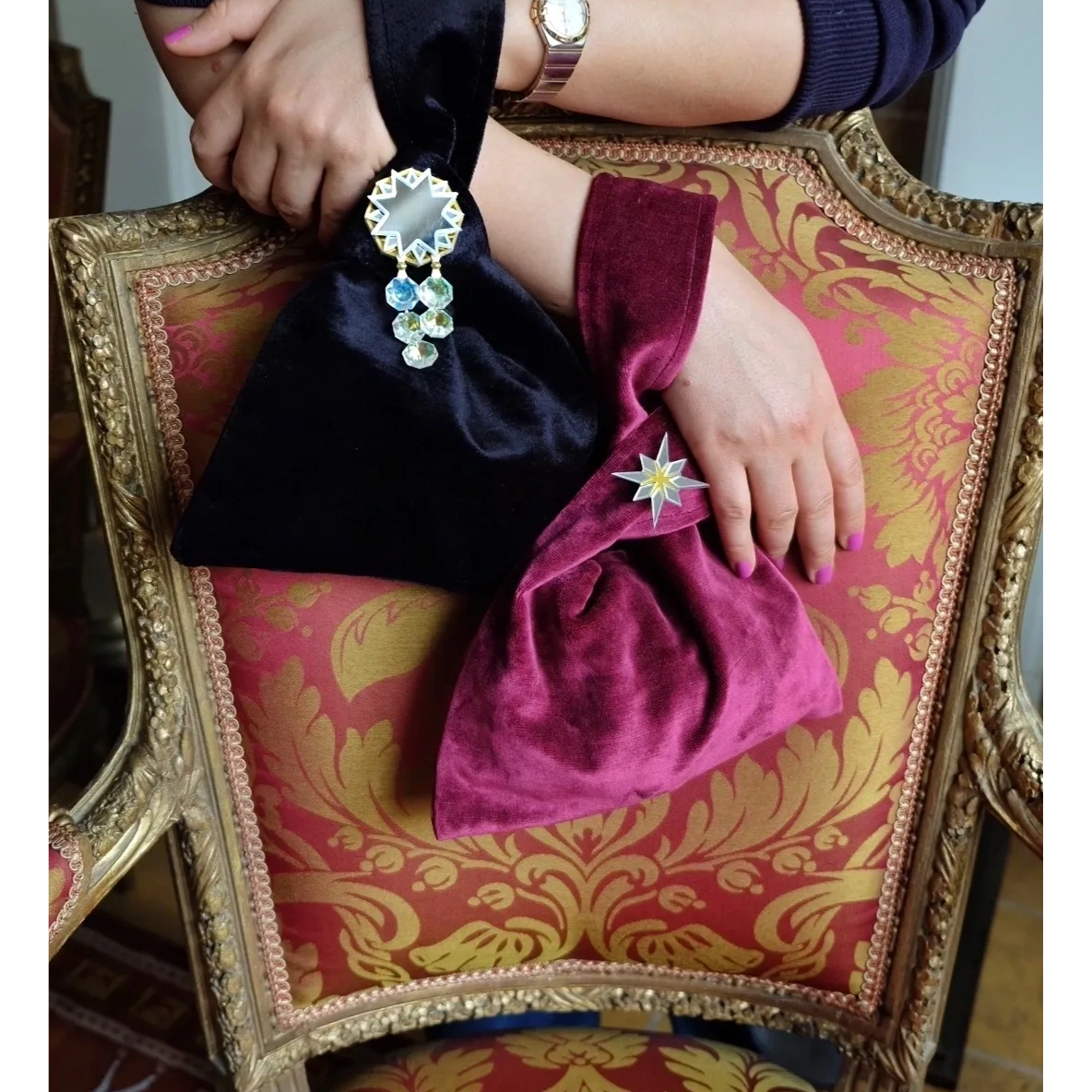 Two velvet handbags with decorative brooches on an ornate chair.