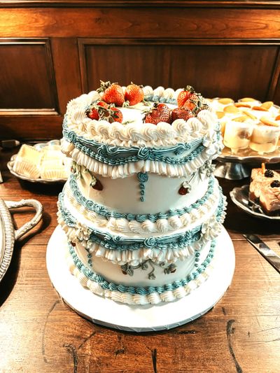 Elegant two-tier cake decorated with strawberries and intricate blue and white icing.