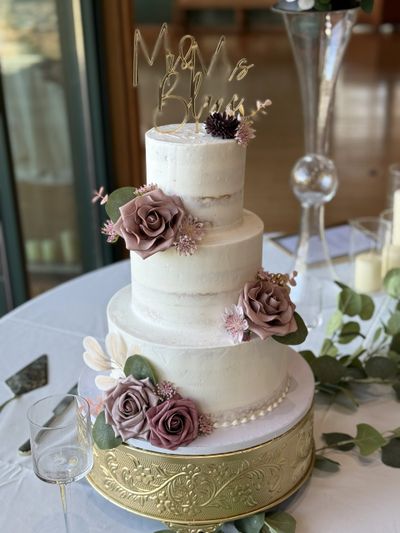 Elegant three-tier white wedding cake with mauve floral decorations and gold topper.