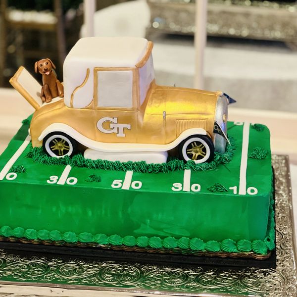 A cake shaped like a vintage gold and white car on a football field with a small dog figure.