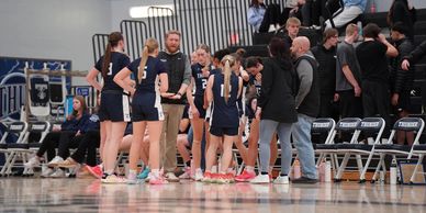 Girls' basketball team huddling with coaches during a timeout.