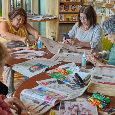 People engaged in arts and crafts around a table with newspapers.