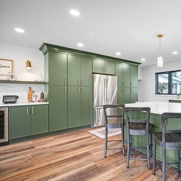 Modern kitchen with green cabinets and wooden chairs around a large island.