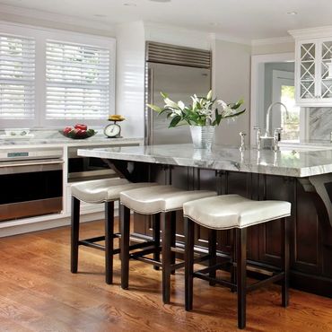 Elegant kitchen with marble countertops, white cabinetry, and dark wood island with stools.