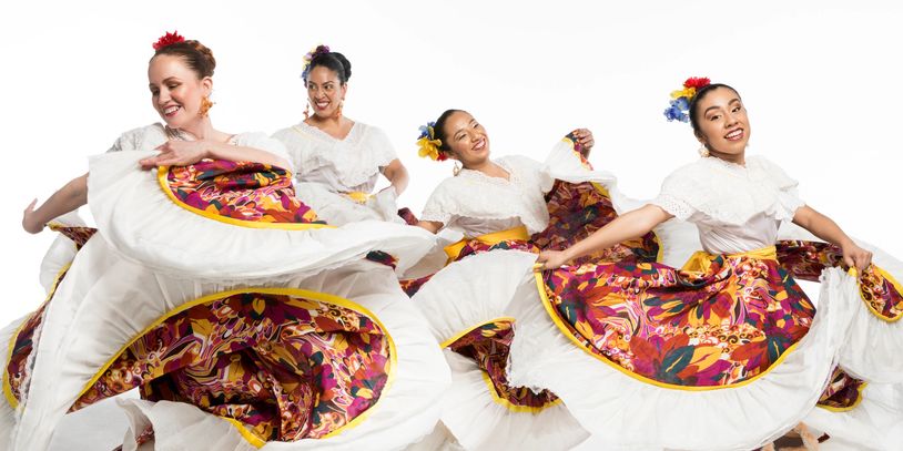 Four women joyfully dancing in vibrant traditional dresses with colorful floral patterns.
