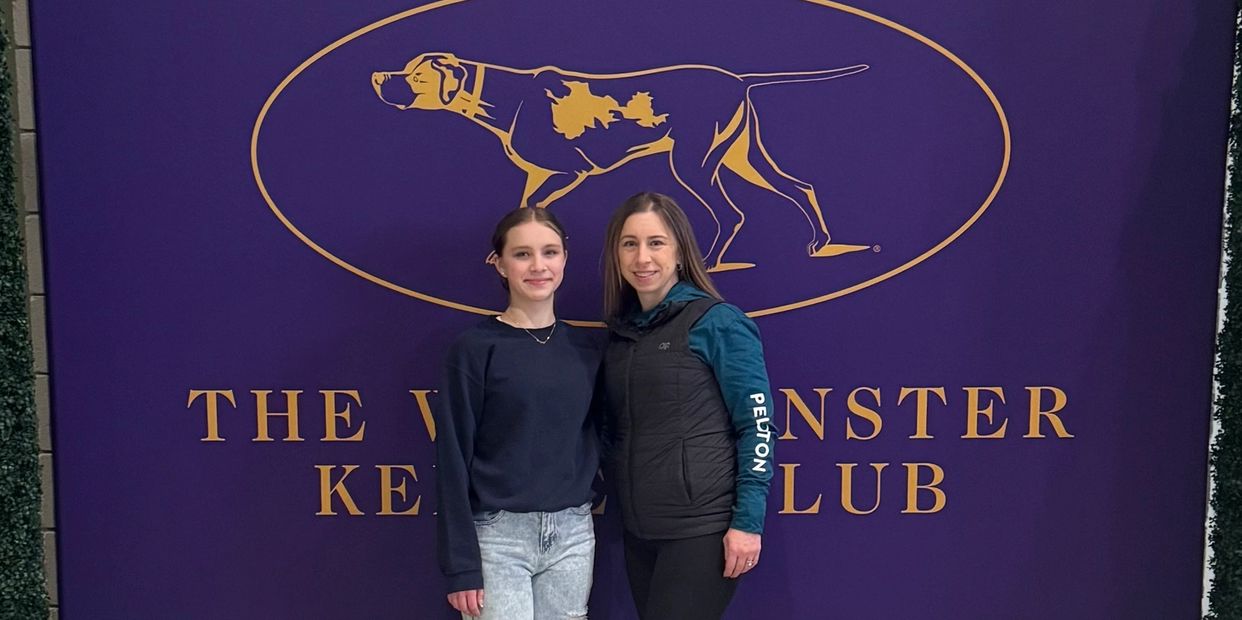 Two women posing in front of a purple Webster Kennel Club banner.