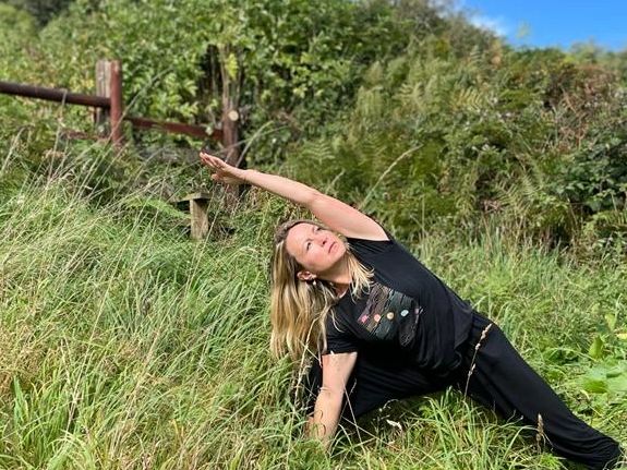 Woman practicing yoga in a grassy field under a blue sky.