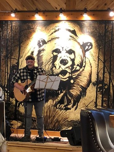 Musician playing guitar in front of a large bear mural.
