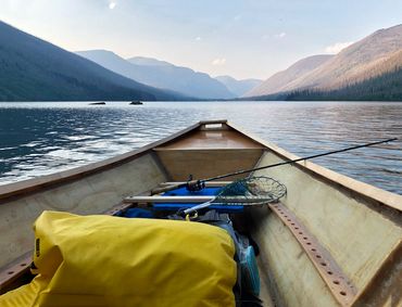 View from a canoe on a serene lake surrounded by mountains at sunset.