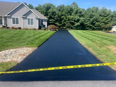 Freshly paved driveway with caution tape in front of a suburban house.