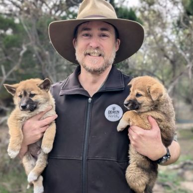 Man holding two fluffy puppies outdoors, smiling.