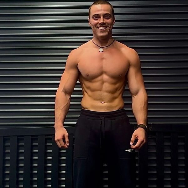 Smiling muscular man showing abs against a dark background.