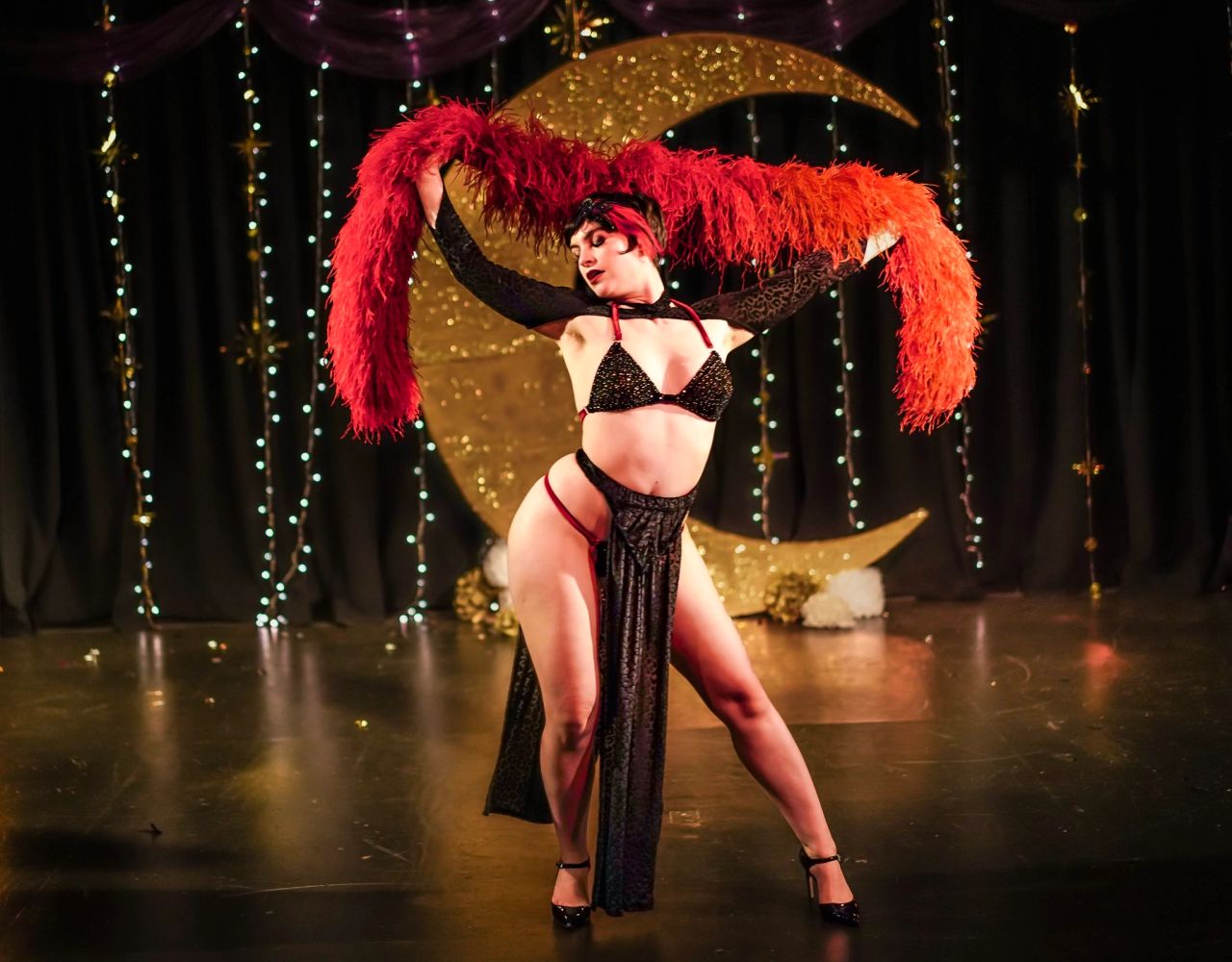 Burlesque dancer in a sparkling outfit with a red feather boa on stage.