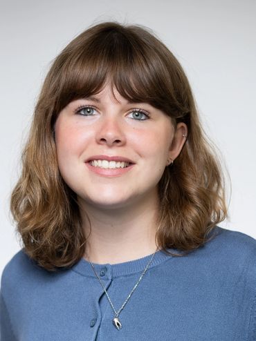 Smiling woman with brown hair and blue cardigan.