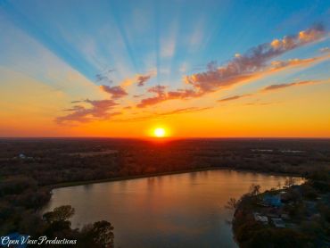 A vibrant sunset over a calm lake with rays of light spreading across the sky.