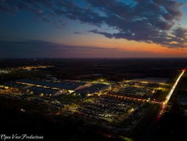 Aerial view of a lit industrial area and parking lot at sunset.