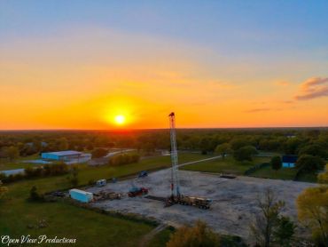 Sunset over a rural drilling site with equipment and trucks.
