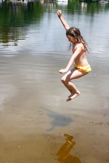 child jumping into water, yellow bathing suit, clear lake water with shadow