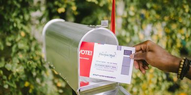 Person placing a mail-in ballot into a mailbox outdoors.