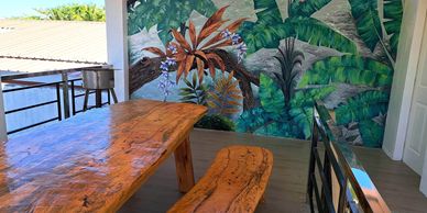 Wooden table and bench set against a vibrant tropical mural.